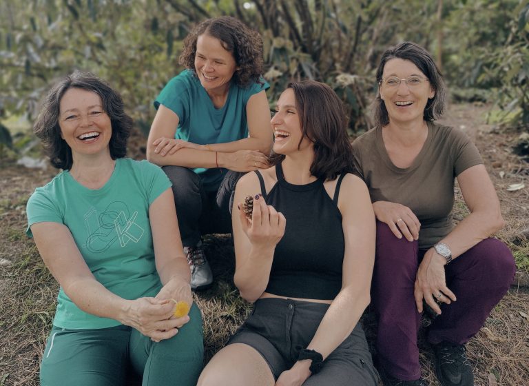 4 Frauen sitzen im Wald und lachen gemeinsam