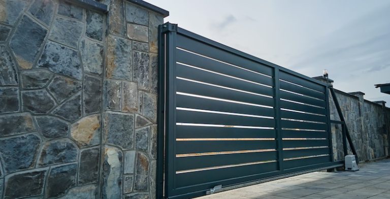 Wide automatic sliding gate with remote control installed in high stone fense wall. Security and protection concept.