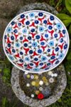 Handmade ceramic fruit bowl with vibrant blue, red and white colored flowers on a white backdrop. Ottoman style design
