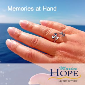 Ring med ankare och propeller på solbränd hand mot himmel och hav. Text: Memories at hand. Marine Hopes logga.