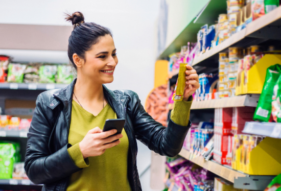 Frau recherchiert mit Smartphone im Supermarkt