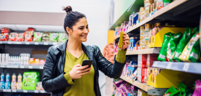 Frau recherchiert mit Smartphone im Supermarkt