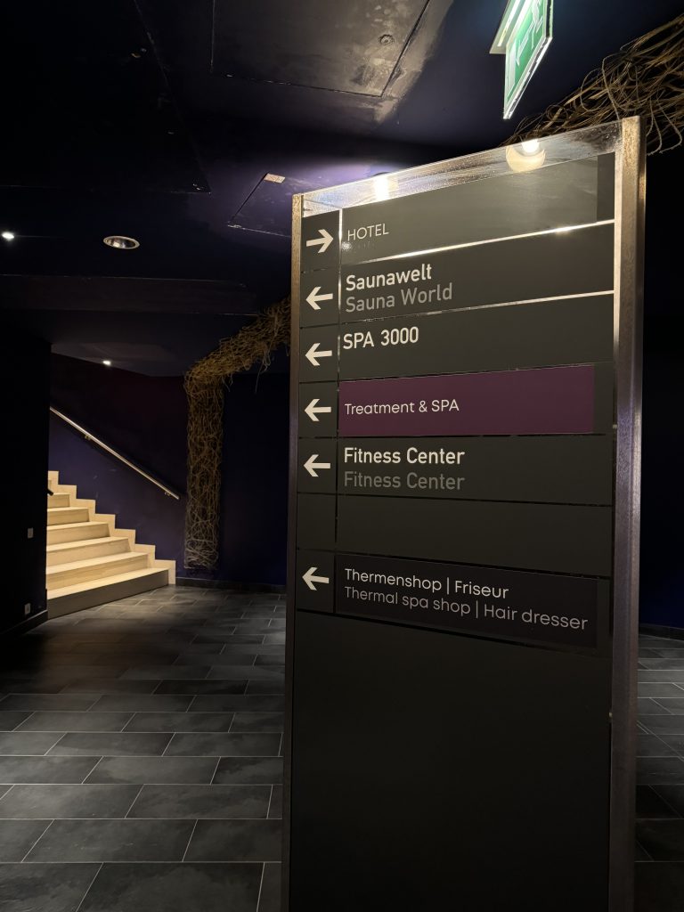 The signposts at the bottom of the purple corridors of the Aqua Dome Therme Längenfeld complex which point to the hotel, sauna world, treatment & spa, fitness center and the Thermal spa shop/hairdresser