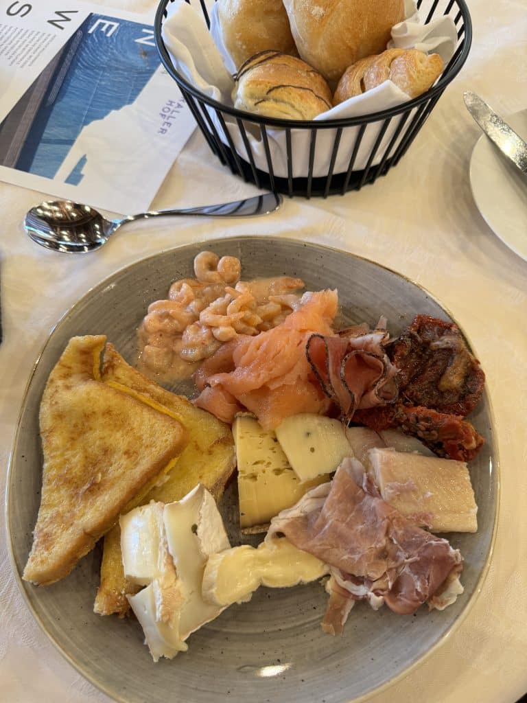 Plate of shrimp salad, fresh salmon, smoked ham, sun-dried tomatoes, several kinds of special cheeses, piece of smoked cod and a basket of pistolets in the breakfast room at the Krallerhof hotel in Austria.