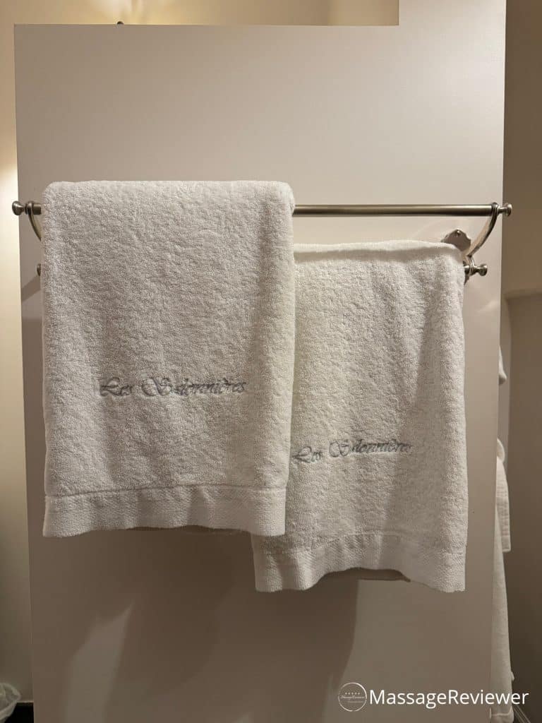 Two white towels with embroidery of the spa's name over a silver rack against the wall at the private spa Les Salonnières in Ouwegem, Belgium