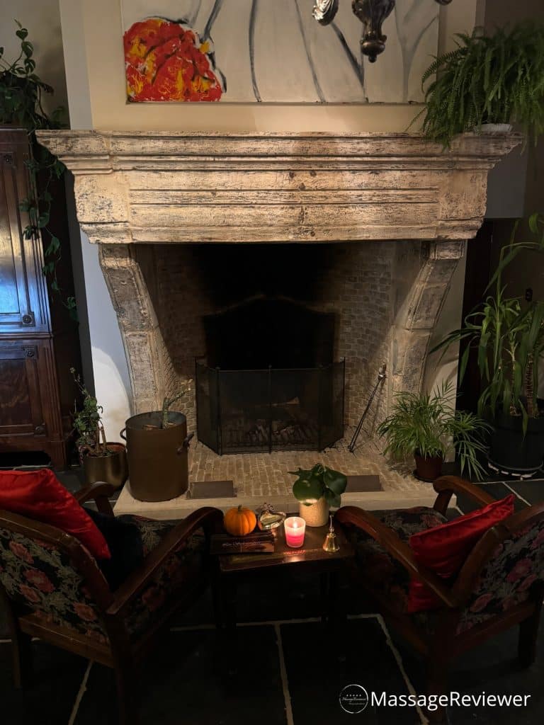 The fireplace place with two wine red velvet seats in front of it in the reception room at the entrance to the private spa Les Salonnières in Ouwegem, Belgium