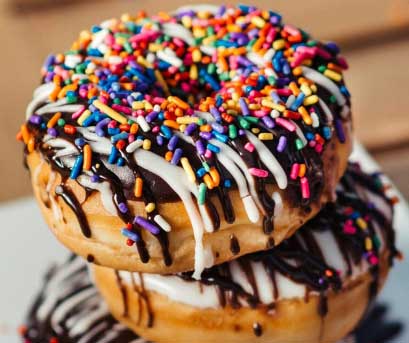 Two chocolate glazed doughnuts with colourful sprinkles on top