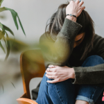 Anxiety, how can naturoapthy help with it? Lady sitting on a chair huddled, holding her head.