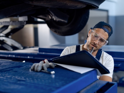 Mid adult mechanic writing notes while examining a car at auto repair shop.