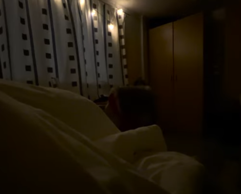 Stillbilde fra et halvmørkt soverom, perspektivet er fra en som ligger i senga.