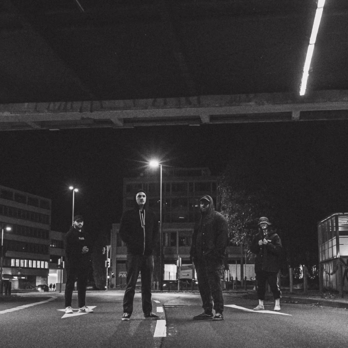 Four grown men standing in the middle of the road at night facing the camera