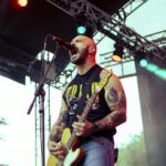 Singer and guitar player of the band Planet of Zeus performing live at Kave Fest. Yellow lights. Singing dramatically.