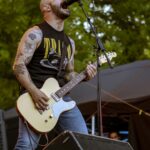 Singer and guitar player of the band Planet of Zeus performing live at Kave Fest. Yellow lights. Singing dramatically.
