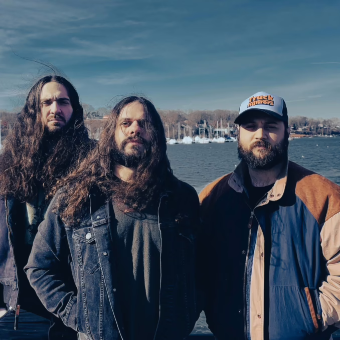 Three band members staring at the camera, ocean/harbor in the background