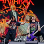 Frank Bello and Joey Belladonna of Anthrax performing live in front of a display of their latest album Cursum Perficio.