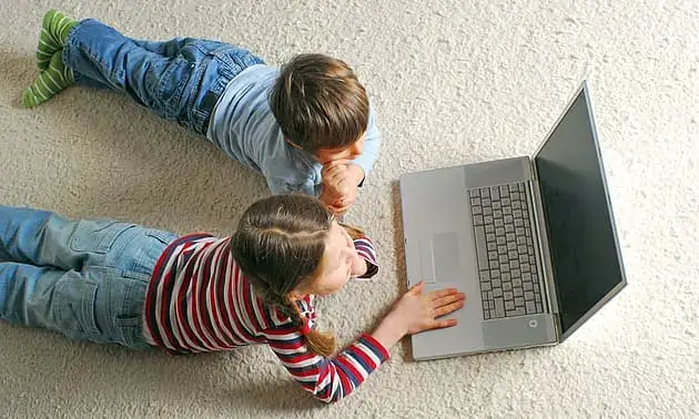 Zwei Kinder liegend auf dem Boden arbeiten an einem Rechner zusammen, um die Emotionale Intelligenz zu steigern.