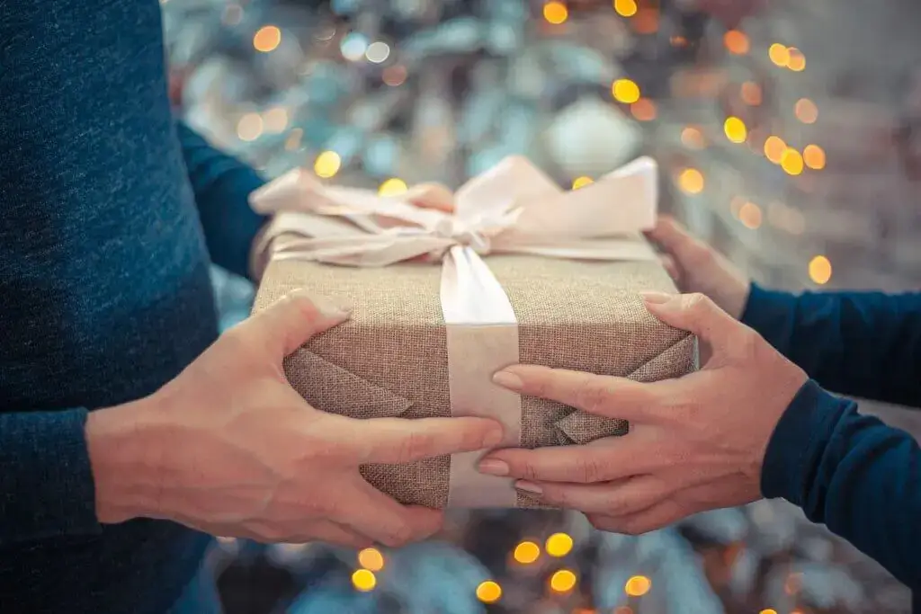 Zwei Menschen halten zusammen ein Geschenk in einem Box mit Lichtern im Hintergrund.