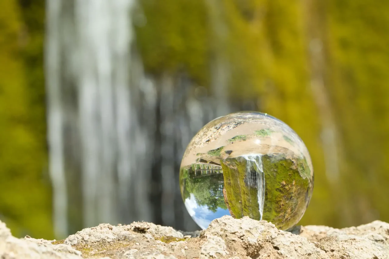 Ein Kugel mit der Erde drinnen steht bei einem Wasserfall in der Natur