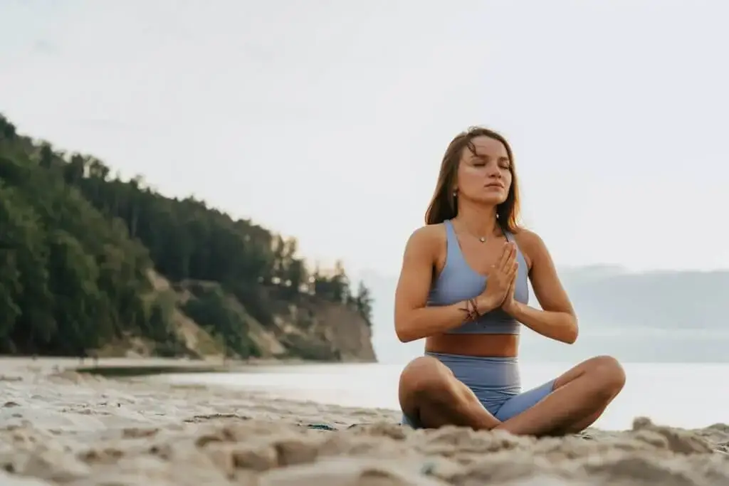 Ein Mädchen, dass auf einem Strand am Meer meditiert, um erfolgreicher zu sein und ihr Ziele im Leben zu verfolgen.