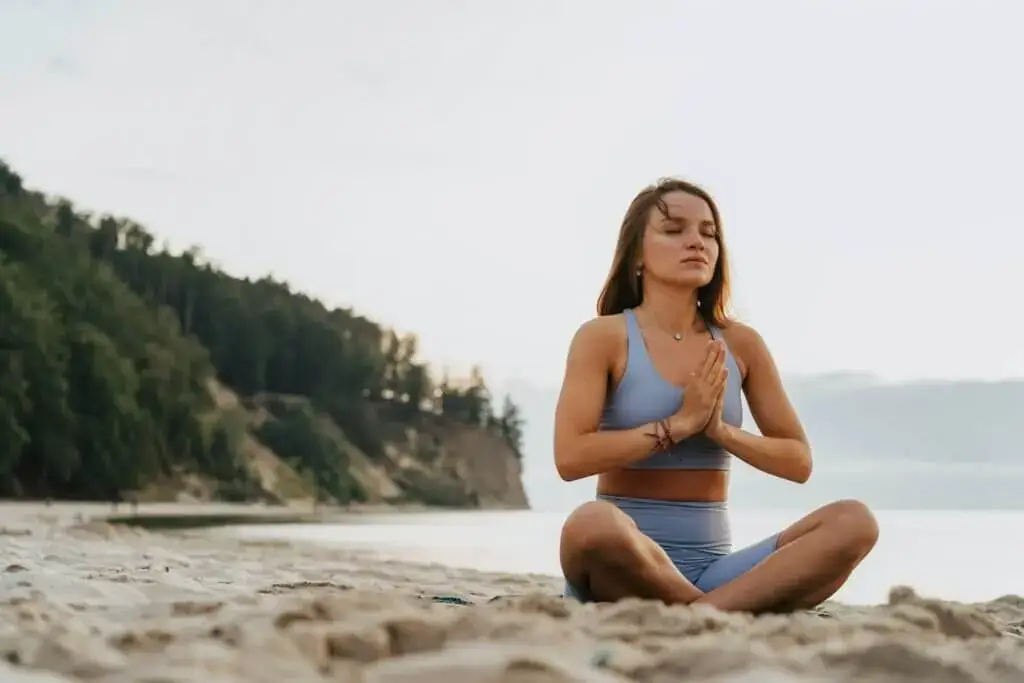 Ein Mädchen meditiert draußen am Meer auf dem Sand, um seinen Geist zu beruhigen.