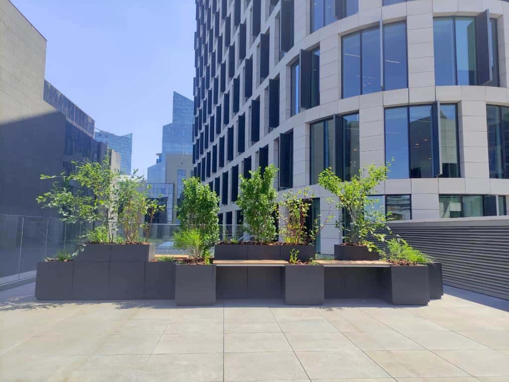 Plantenbakken in speciaal design met zitbanken zorgen voor groen accent en bakenen zones op esplanade naast modern kantoorgebouw af