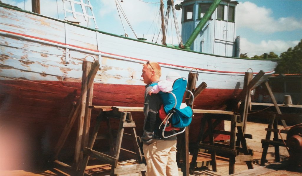 Dänemark Mann mit kind in der Kraxe vor einem Boot im Museum