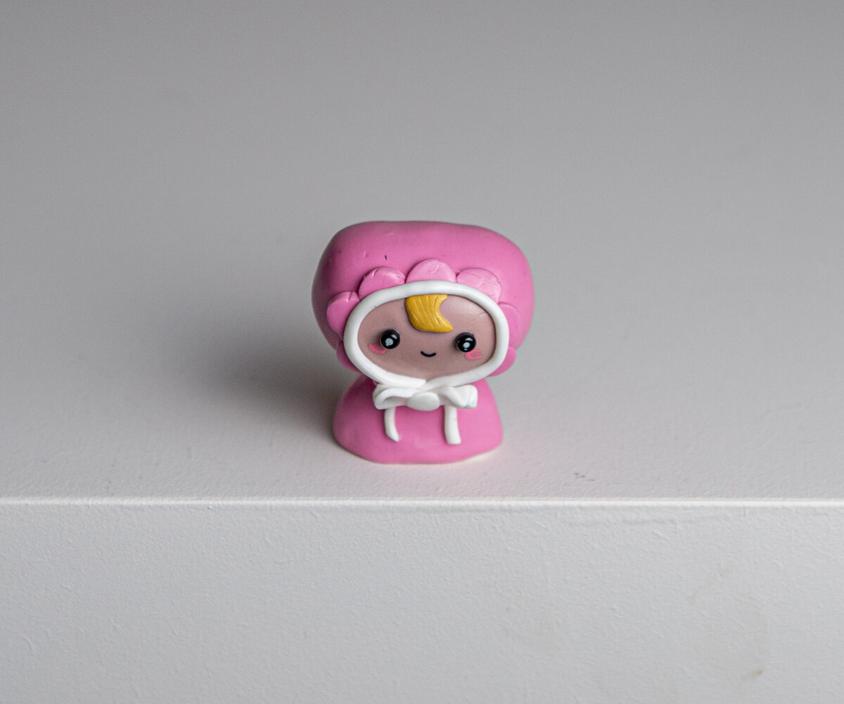 A polymer clay figurine wearing a pink bonnet with lace by Mitsuo
