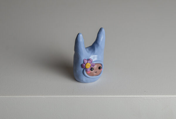 A polymer clay figurine wearing a blue bunny hat and a flower by Mitsuo