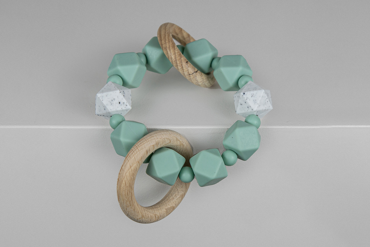 A turquoise and speckled white silicone baby teether with wooden rings by Mitsuo