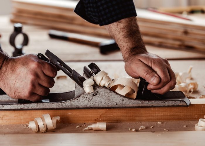 carpenter's hands planing a plank of wood with a hand plane