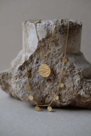 the Alceste Necklace by the brand Agapé Studio, shown on a rock, combined with the Scorpio Necklace