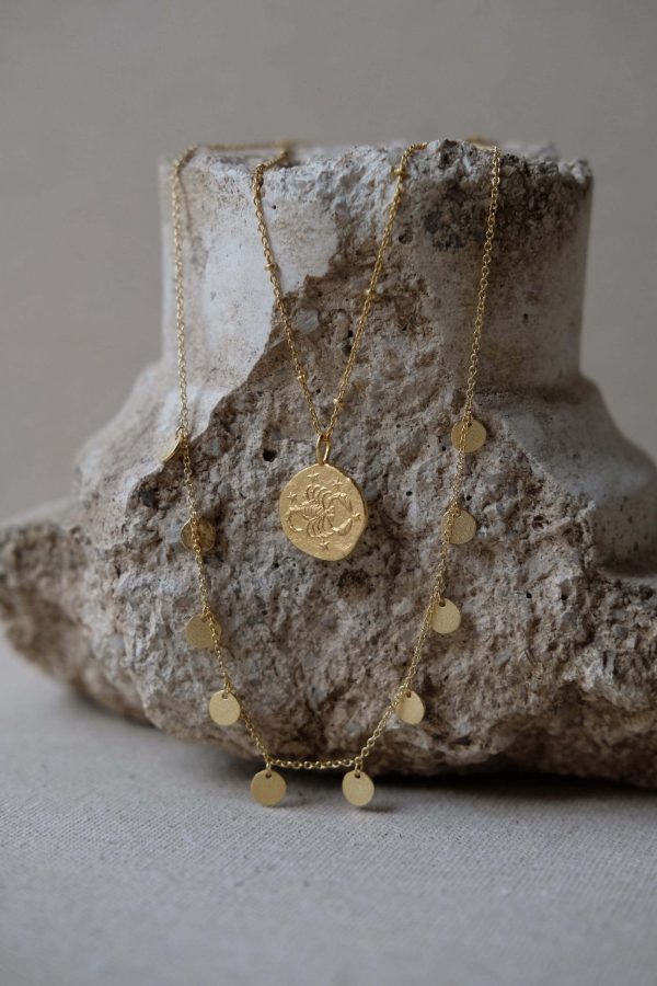 the Alceste Necklace by the brand Agapé Studio, shown on a rock, combined with another pendant necklace