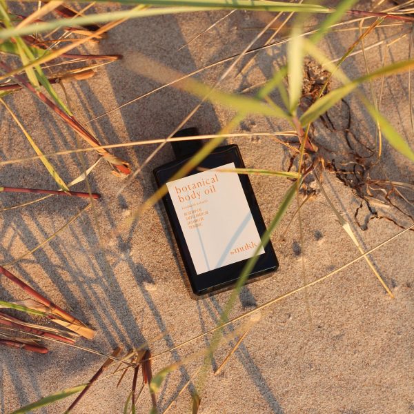 the Botanical Body Oil by By Mukk shown on the beach, because nature is the designers' biggest inspiration