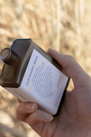 Someone holding an open bottle of Cleansing Milk in their hand, showing the milky consistency of the product