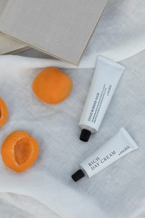 the Good Barrier Mask of By Mukk styled next to a few apricots which is one of the product's main active ingredients