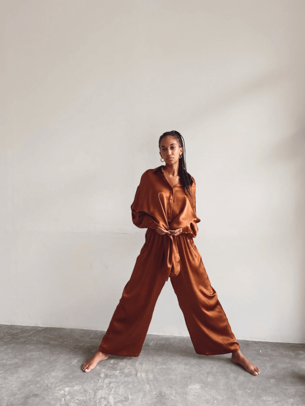a woman is effortlessly wearing the Jai Button Up in Coco by the brand Bahhgoose, styled with the matching pant, showing the soft and bright fabric