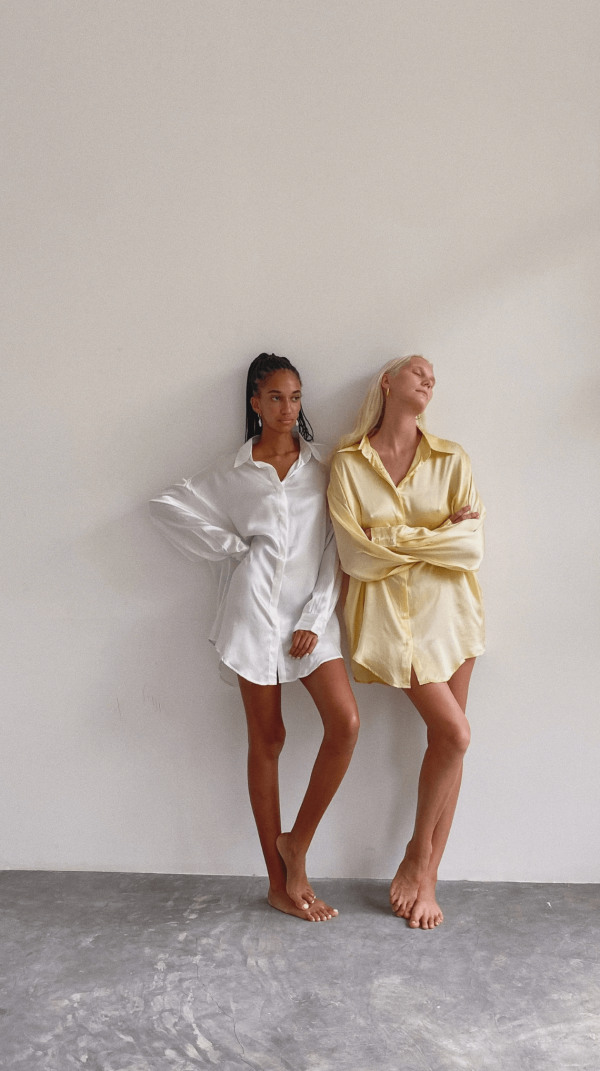 two women wearing the Jai Button Up shirts in white and yellow, by the brand Bahhgoose, styled as dresses