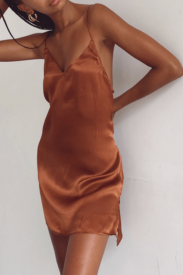 a woman leaning against a wall while wearing the Jai Dress in Coco by the brand Bahhgoose, showing the relaxed fit and soft silky fabric of the dress