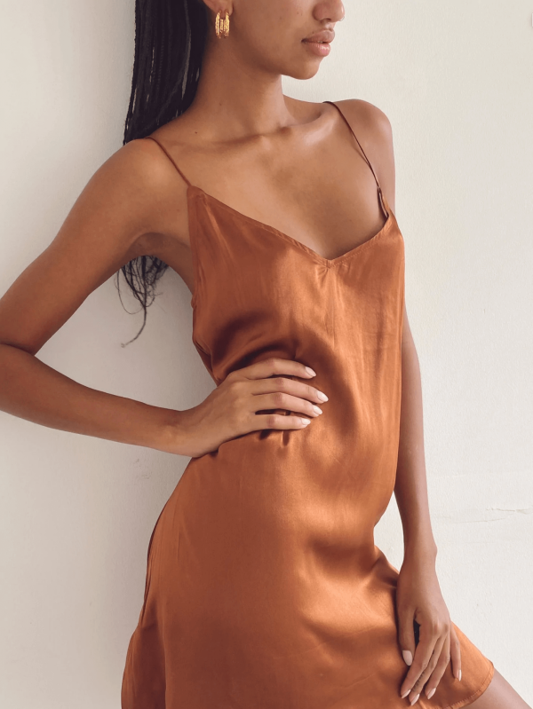 a woman leaning against a wall while wearing the Jai Dress in Coco by the brand Bahhgoose, showing the relaxed fit and soft silky fabric of the dress