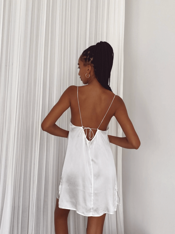 back view of a woman wearing the Jai Dress in White by the brand Bahhgoose, showing the adjustable tie straps and the open back of the dress