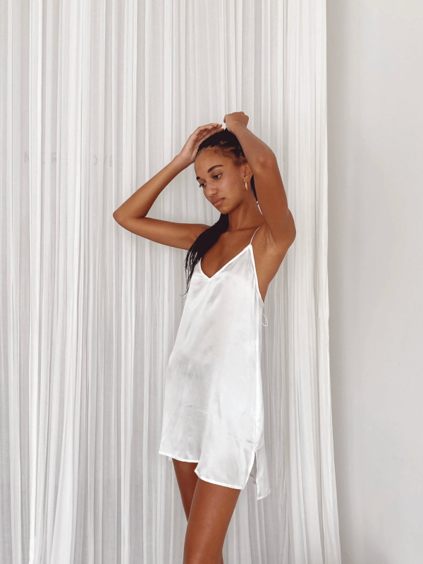 a woman standing while wearing the Jai Dress in White by the brand Bahhgoose, showing the relaxed yet refined look of the dress