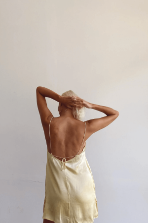 back view of a woman wearing the Jai Dress in Yellow by the brand Bahhgoose, showing the adjustable tie straps and the open back of the dress