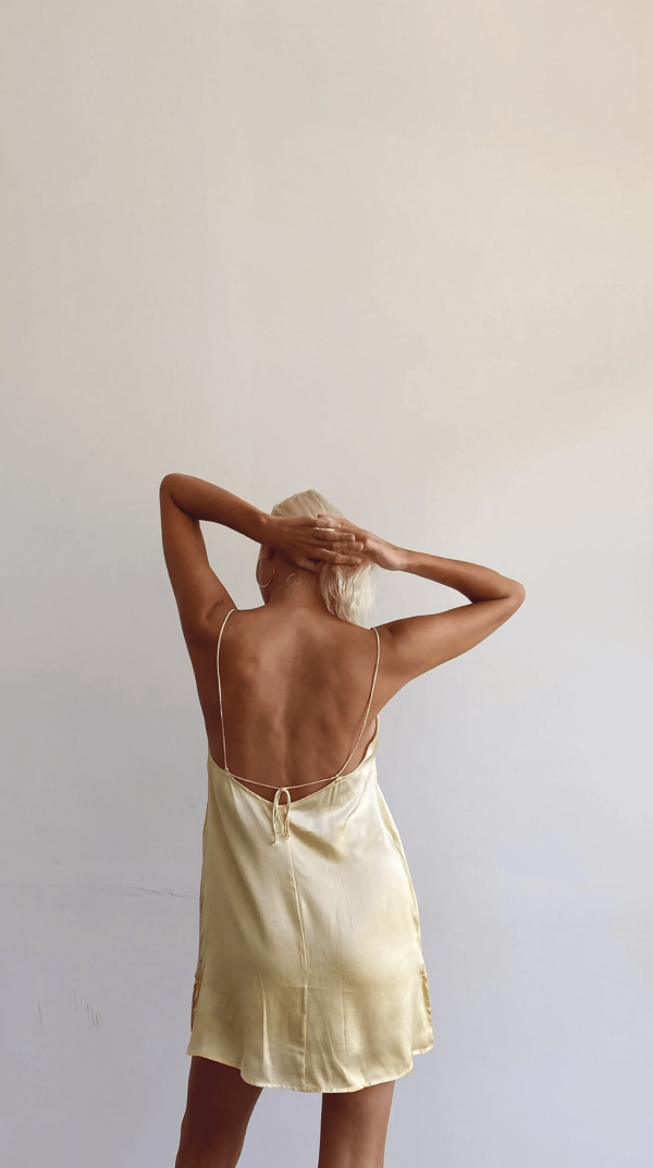 back view of a woman wearing the Jai Dress in Yellow by the brand Bahhgoose, showing the adjustable tie straps and the open back of the dress
