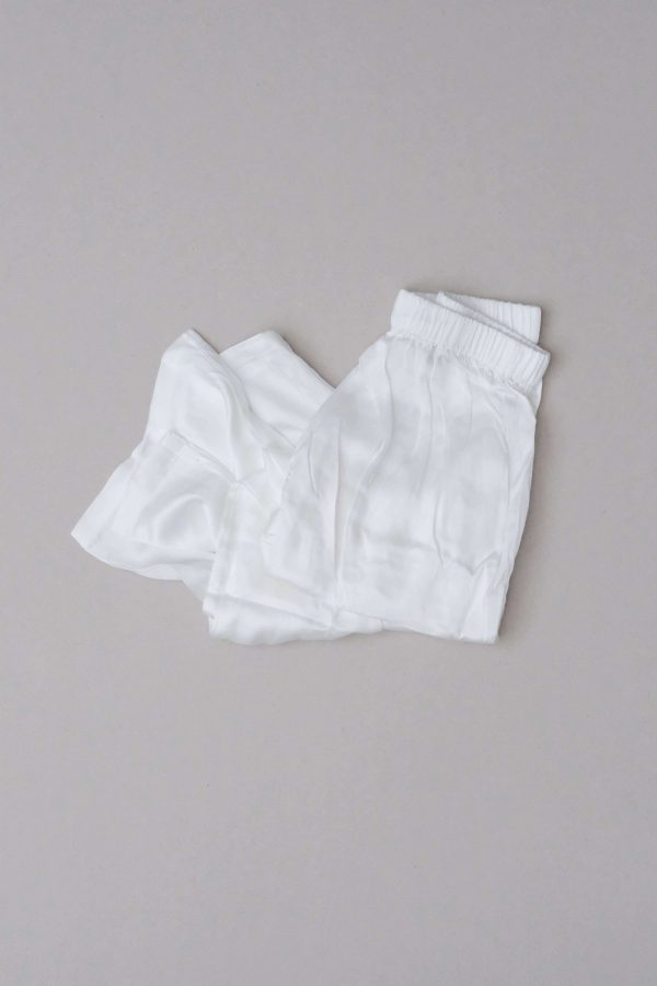 Flatlay of the folded silk Jai Pant in White by the brand Bahhgoose, showing the stretchy waistband and the silk fabric