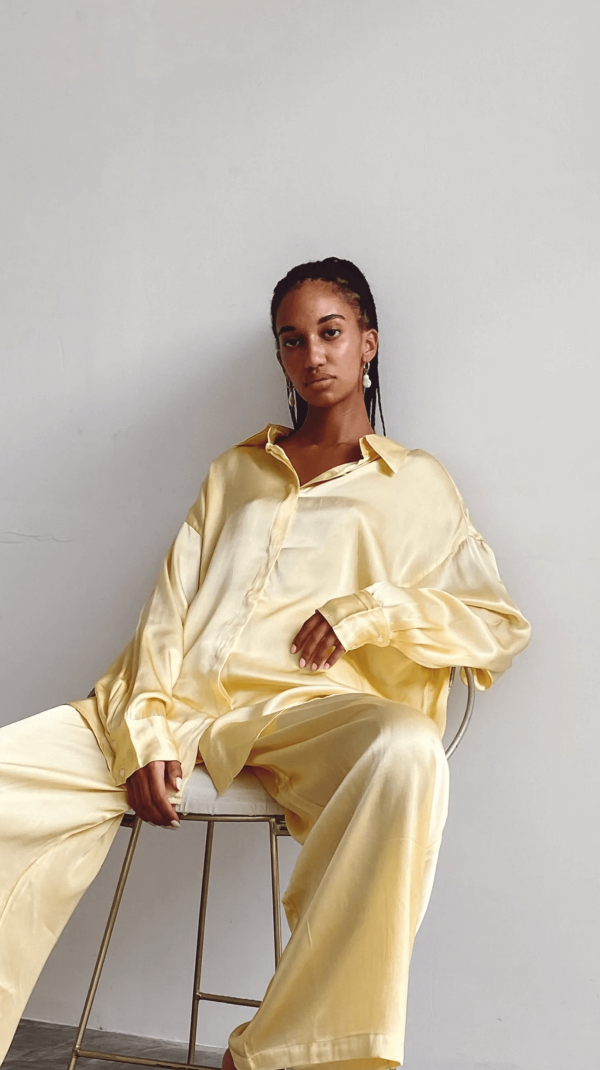 woman sitting down while wearing the Jai Pants with matching Jai Button Up in Yellow by the brand Bahhgoose, showing the relaxed fit of the co-ord set