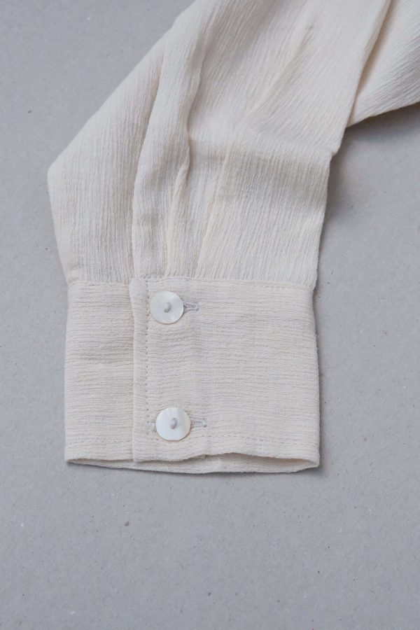 detailed flatlay of the Ker Button Up in Natural by the brand Bahhgoose, showing the cuff sleeve and the textured fabric