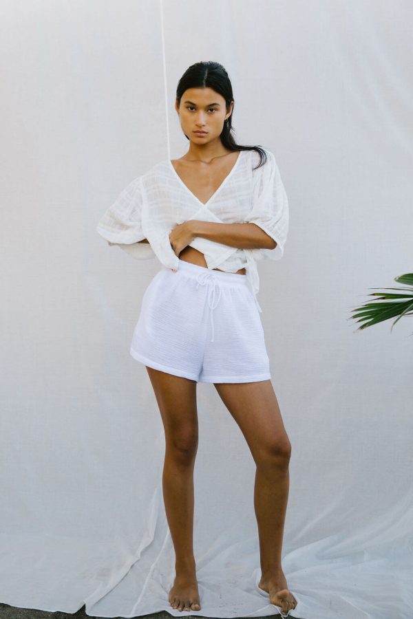 woman wearing the Ella Wrap Top in White Textured paired with the Maddie Shorts by the brand The Bare Road