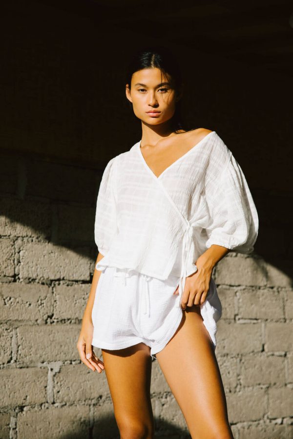 woman wearing the Ella Wrap Top in White Textured paired with the Maddie Shorts by the brand The Bare Road