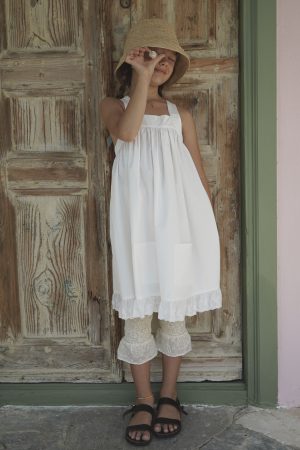 girl wearing the Frida Apron Dress in Cotton D'éte fabric, paired with the Zadie Pants in Creme Broderie by the sustainable brand House of Paloma, curated by Morsel Store