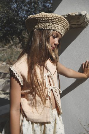 girl wearing the Pasquelina Vest in muslin Peach Sorbet fabric paired with the Camille Skirt in a floral Fleur Bleue and a raffia hat by the sustainable brand House of Paloma, curated by Morsel Store